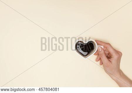 Woman Hands Holds Heart Shaped Cup Of Coffee. Black Hot Coffee In A White Heart-shaped Cup.