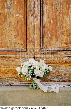Bouquet Of White Roses Tied With A Ribbon Stands On The Threshold Of A Wooden Door