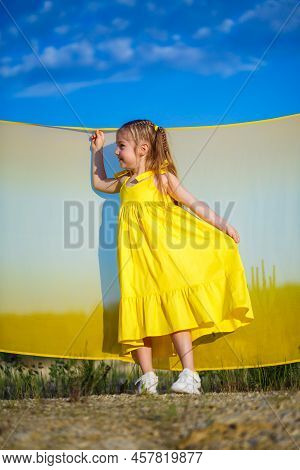 Ukrainian Girl 7 Years Old, She Is A Patriot Of Ukraine, Dressed In A Yellow Dress Against A Blue Sk