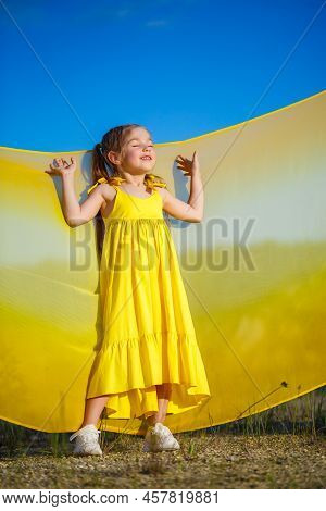 Ukrainian Girl 7 Years Old, She Is A Patriot Of Ukraine, Dressed In A Yellow Dress Against A Blue Sk