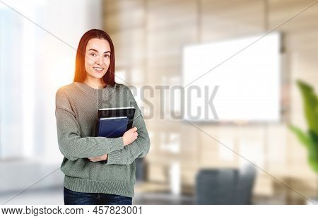 Attractive Businesswoman Wearing Casual Wear Is Standing Holding Notebook At Office Workplace In Bac