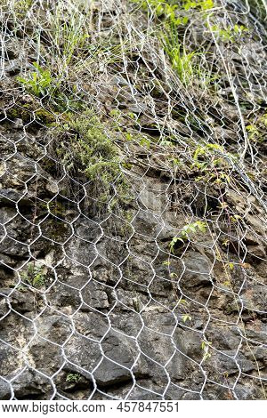 Natural Rock With Mesh To Protect Against Landslides Dangerously Sliding Down The Cliff Onto The Roa