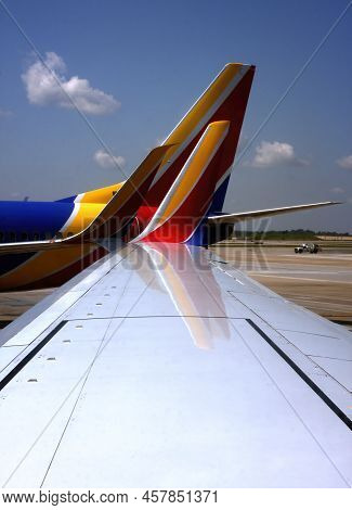 Wingspan Of Airplane Contrasts With The Colors Of A Neighboring Plane At The Terminal Gate