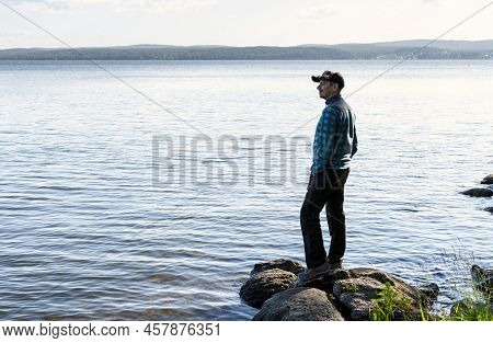 Young Man In A Cap Looking At The View Of The Lake Or River Standing On The Stones Enjoying Nature L