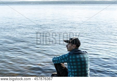Young Man In A Cap Looking At The View Of The Lake Or River Sitting On The Stones Enjoying Nature La