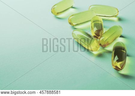 Fish Oil. Yellow Softgels Lie On A Green Surface. Vitamins And A Healthy Lifestyle. Background Or Ba