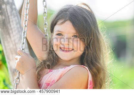 Happy Child Girl Laughing And Swinging On A Swing At Summer Garden. Happy Kid Having Fun Outdoors. C