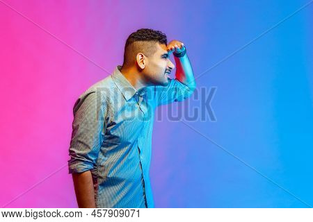 Side View Portrait Of Calm Attentive Man In Shirt Standing Holding Hand Over Eyes And Looking Far Aw