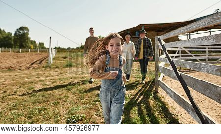 Selective Focus Of Smling Little Girl Run While Her Blurred Grandparents And Brother Walk On Backgro
