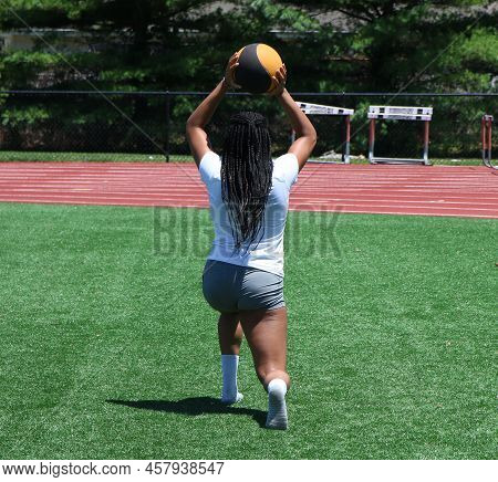 Rear View Of African American Girls Performing Wallking Lunges While Holding A Medicine Ball Over He