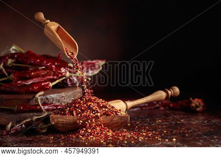 Chilli Flakes Are Poured Into A Wooden Dish. Chilli Flakes And Dried Chili Peppers On A Brown Backgr