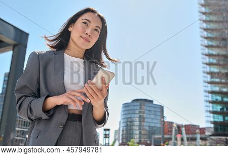 Young Asian Businesswoman Wearing Suit Holding Mobile Phone Standing In Big City On Busy Downtown St