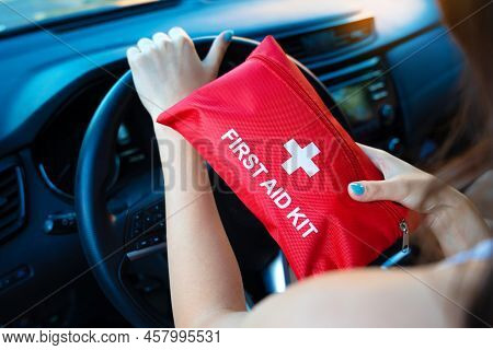 Car First Aid Kit In Female Hands On A Steering Wheel Background. Road Accident, Preparing For A Roa