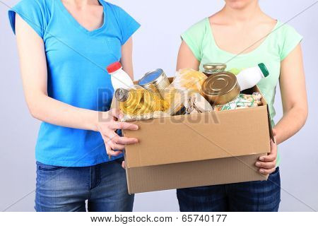 Volunteers with donation box with foodstuffs on grey background