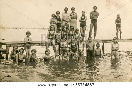 AUGUSTOW, POLAND, CIRCA 1950s: Vintage photo of group of children resting on lakeside with their tutors