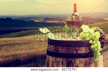 Red wine bottle and wine glass on wodden barrel. Beautiful Tuscany background