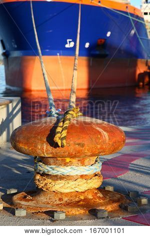 Close up of a port bollard with commercial freight ship mooring lines tied to keep the ship at anchor.