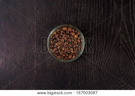 Coffee beans in a glass bowl - top view. On a black background. Still life. Copy space