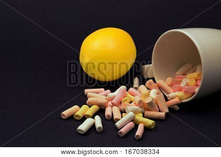 Coloured marshmallows spilled from a mug on dark background with lemon