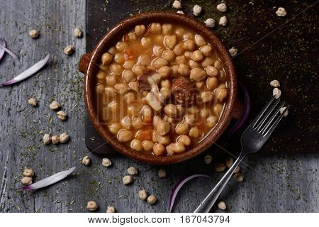 high-angle shot of an earthenware bowl with spanish cocido madrileno, a stew typical of madrid with chickpeas and other vegetables, chorizo, pork, bacon and ham, on a rustic wooden table