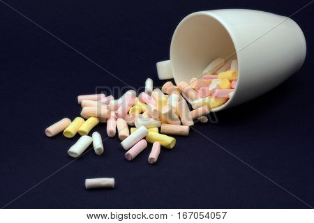 Coloured marshmallows spilled from a mug on dark background
