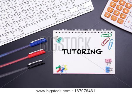 KEYBOARD, PENS WITH WORD TUTORING AT NOTEBOOK ON BLACK BACKGROUND