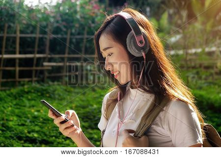 Asian hipster cute teen girl with backpack listening to the music with headphones lying on peak. Tourist traveler on background valley landscape view mock-up sunlight in trip in basque country