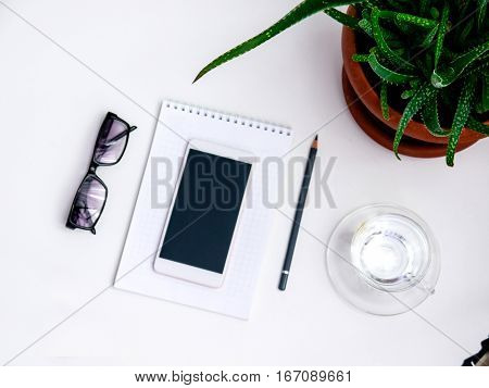 Minimal white office desk table  glass of drinking water and flower pot. Top view with copy space, flat lay.