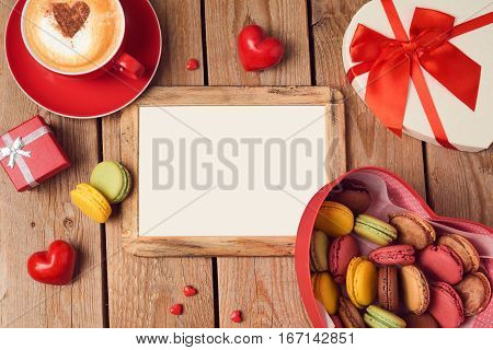 Valentines day concept with macarons coffee cup and blank photo frame over wooden background. Top view from above