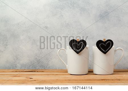 Valentines day concept with coffee cups and chalkboard heart shapes on wooden table