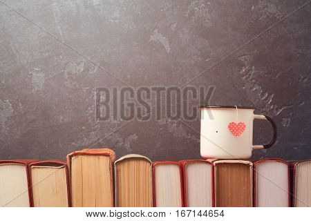 Valentines day concept with retro tea cup on books over blackboard background