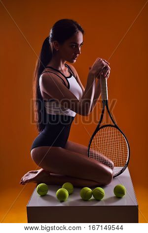 Young sexy tennis player woman sitting on orange background