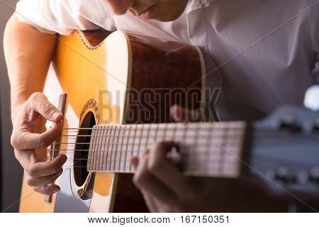 A man sitting and playing classic wooden guitar close up to chord tab fretboard.