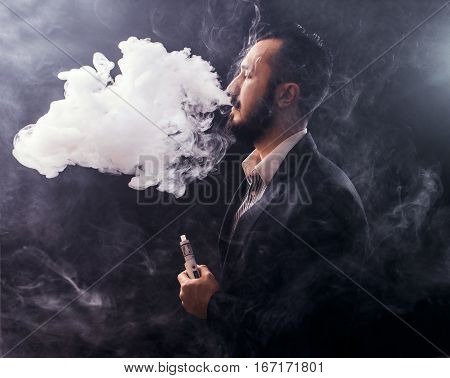 Vaping Man Holding A Mod. A Cloud Of Vapor. Black Background.