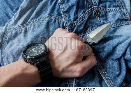 Serrated Knife On Jeans Background In Left Hand.