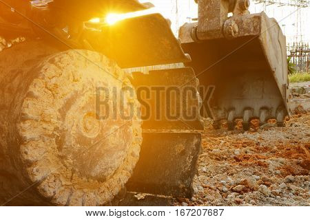 Detail of caterpillar track wheels and bucket on the ground in construction site at sunlight.