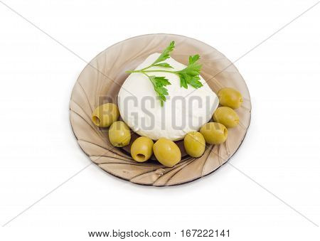 Ball of the fresh soaked mozzarella cheese with twig of parsley and several green olives on the glass saucer on a light background