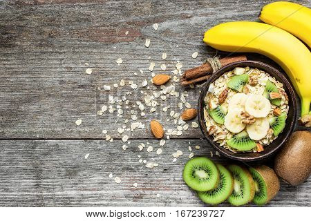 healthy breakfast. homemade muesli with oat kiwi fruit banana nuts and cinnamon in a bowl over rustic wooden background with copy space. top view