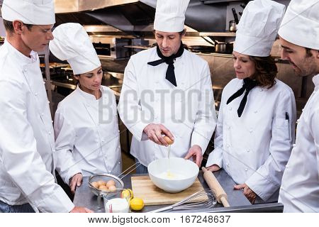 Head chef in commercial kitchen teaching his team to prepare a dough
