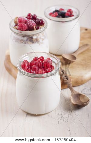 Homemade yogurt with frozen berries red currants black currants raspberries and cranberries in three banks
