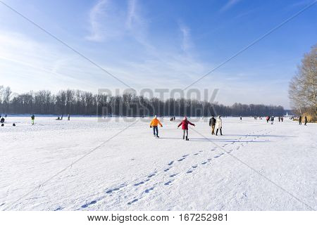 View on happy People on a frozen Lake.
Sporty People  with ice skates. Sunny Winter Day.
Kuhsee in Winter. Germany. Winter Landscape in Bavaria.