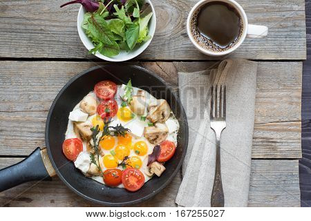 fried eggs in a black pan with mushrooms and cherry tomatoes and cup of coffee
