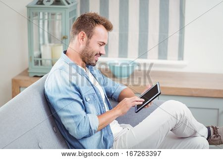 Young man smiling while using digital tablet on sofa at home
