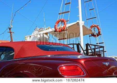 ELOUNDA, CRETE - SEPTEMBER 17, 2016 - Red soft topped Bentley Continental car with a yacht to the rear Elounda Crete Greece Europe, September 17 2016.