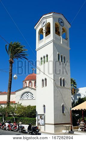 ELOUNDA, CRETE - SEPTEMBER 17, 2016 - Clock tower with a Greek church to the rear in the town centre Elounda Crete Greece Europe, September 17, 2016.