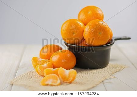 Group of tangerines in a small black bowl and peeled mandarin in the foreground.