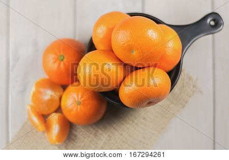Group of tangerines in a small black bowl and peeled mandarin in the foreground.