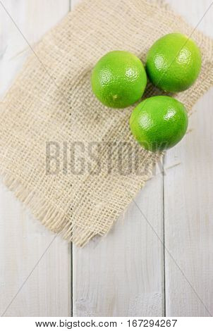 Three lime on the piece of cloth from a sacking on a wooden table.