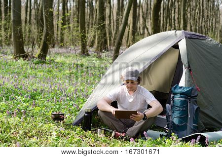 Backpacker uses a tablet outdoors in freen forest.