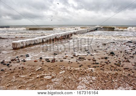 breakwater covered by ice breaking waves on cold gloomy winter day closeup